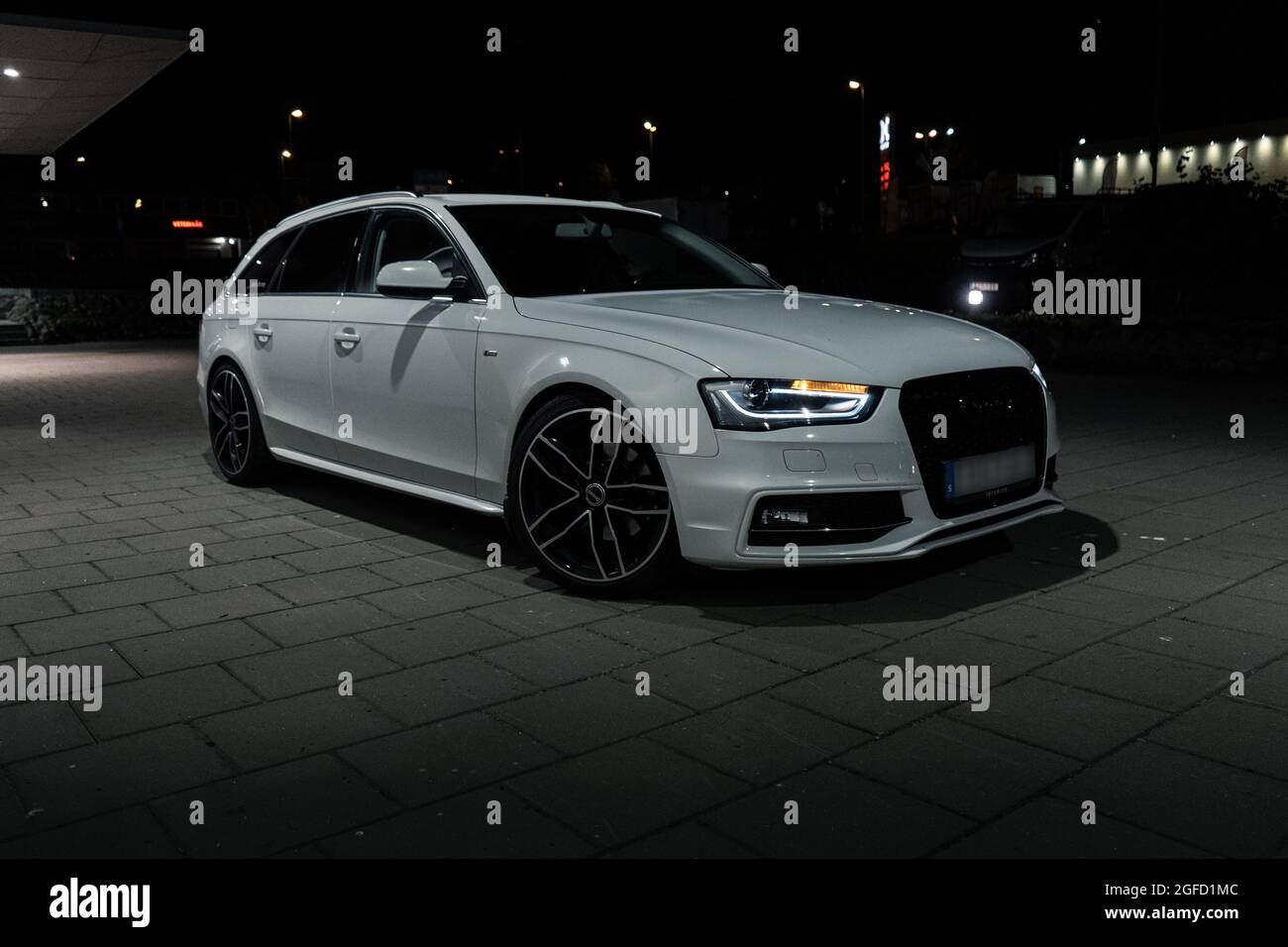 ULRICEHAMN, SWEDEN - Aug 04, 2021: The front part of white Audi A4 Avant with lit headlights outdoors at night Stock Photo