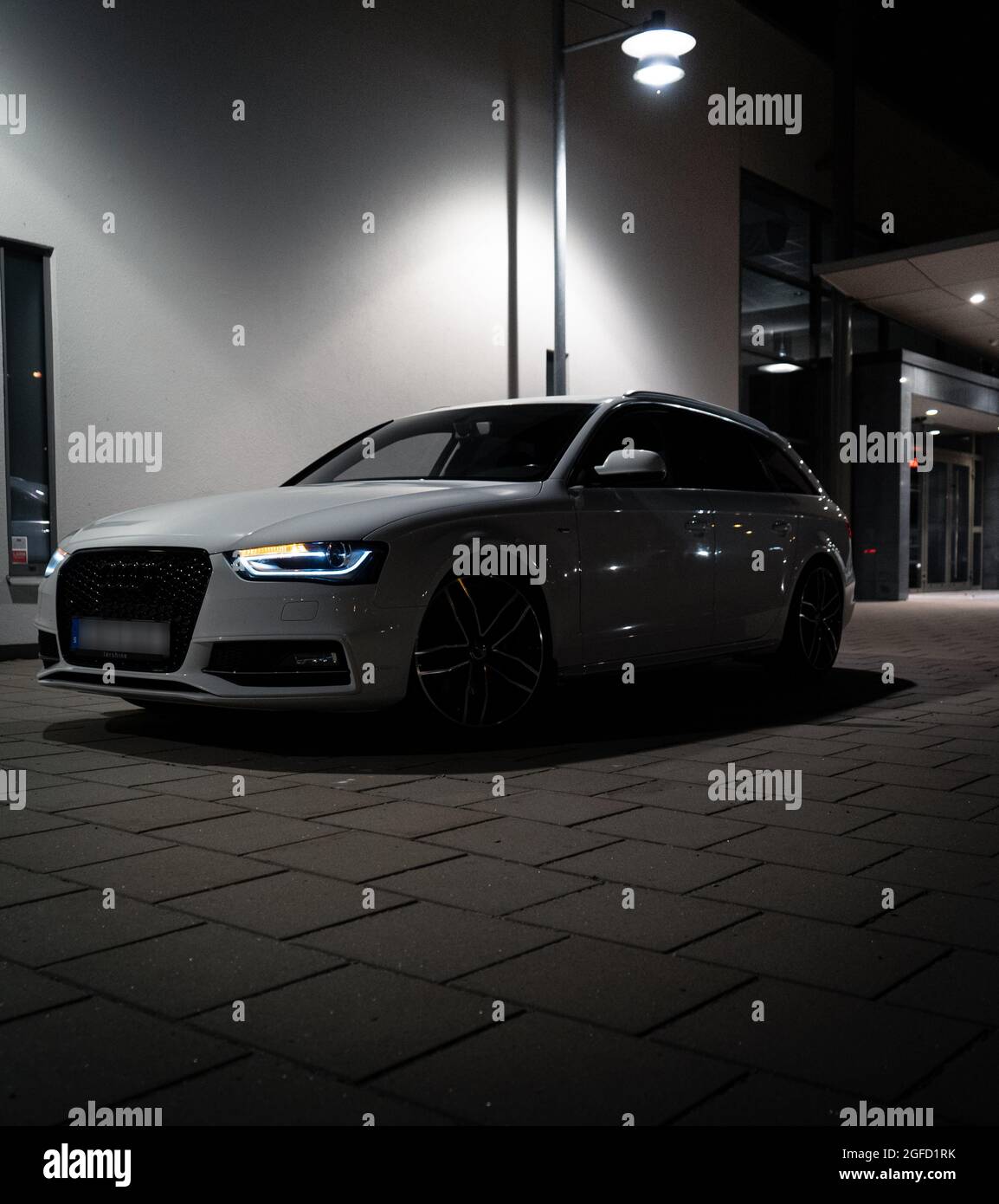 U, SWEDEN - Aug 05, 2021: The front part of white Audi A4 Avant with lit headlights outdoors at night Stock Photo