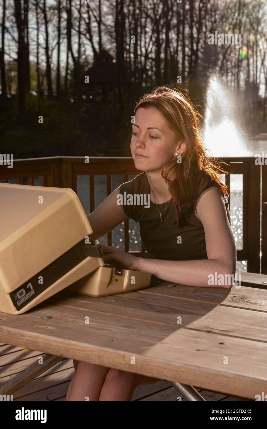 A young woman works diligently on her 1980s era Osborn computer, a sleek reminder of the 'luggable' era of computing. Stock Photo
