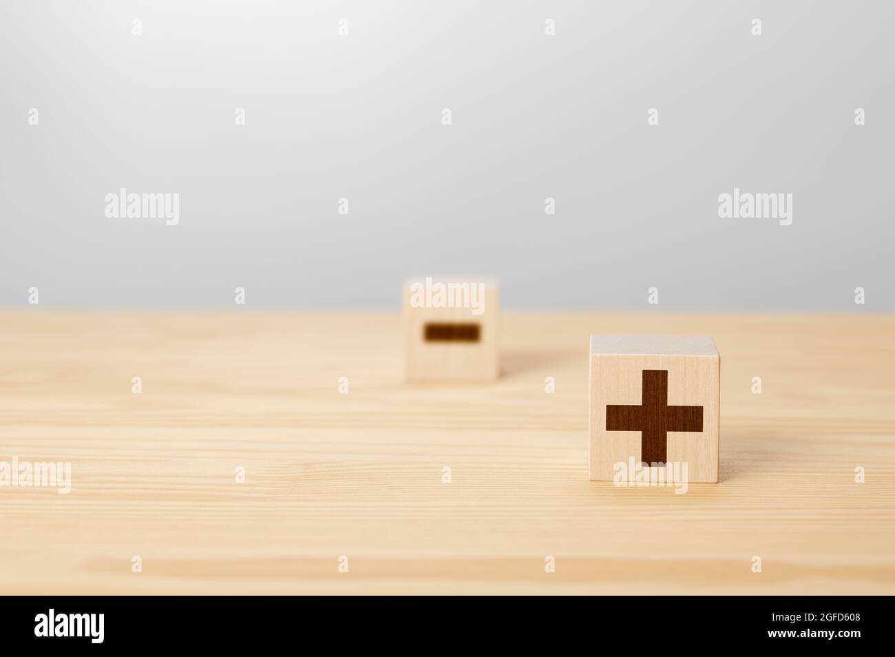 Pros and cons concept. Choosing plus with blurred minus symbol. concept of opposites, wood block with plus and minus on gray background, wooden cubes Stock Photo