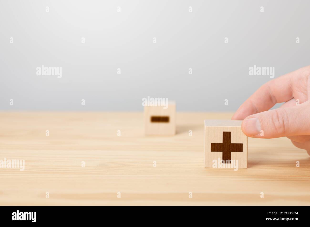 Person Holding Plus Sign Block Against Minus. Plus or minus. man hold cube with plus icon. hand choose wood cube with plus sign. blurred wooden cube w Stock Photo