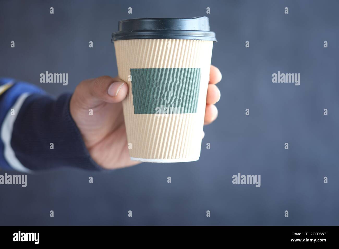hand holding take away paper cup against black background. Stock Photo