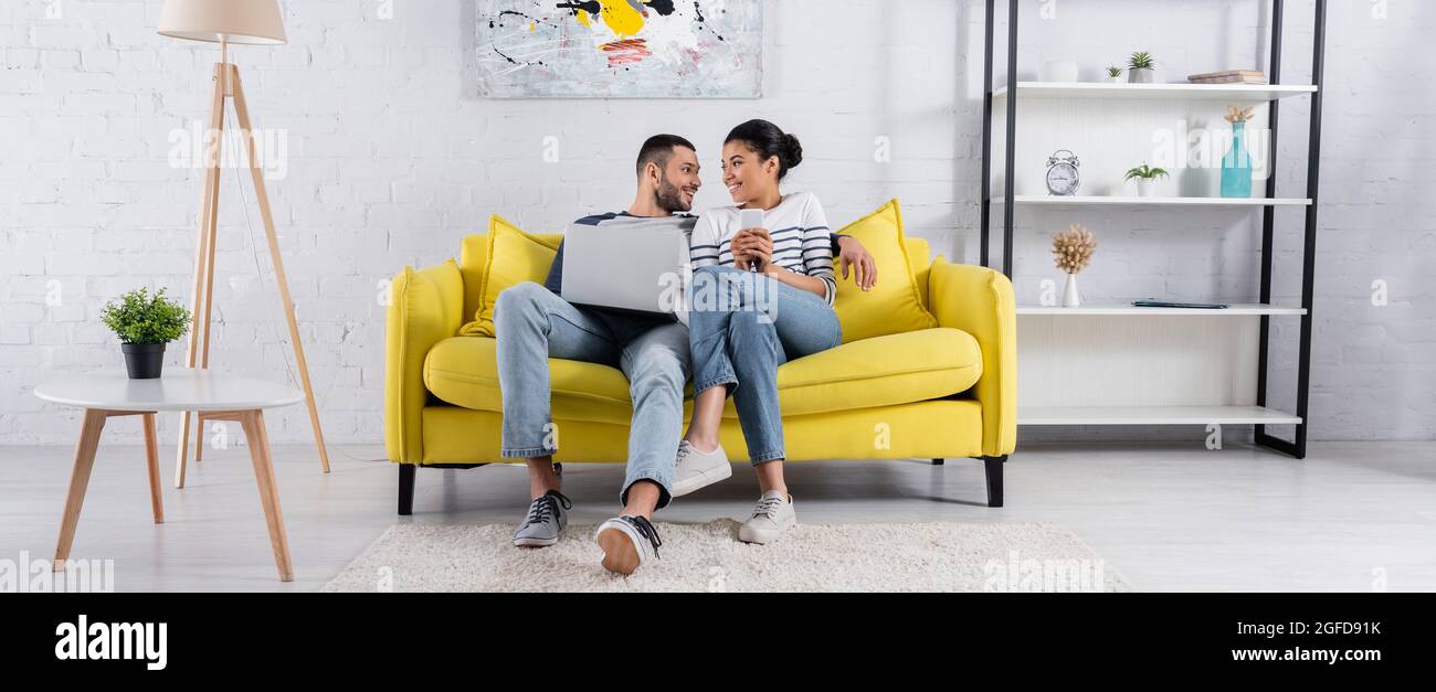Young multiethnic couple using gadgets on couch, banner Stock Photo