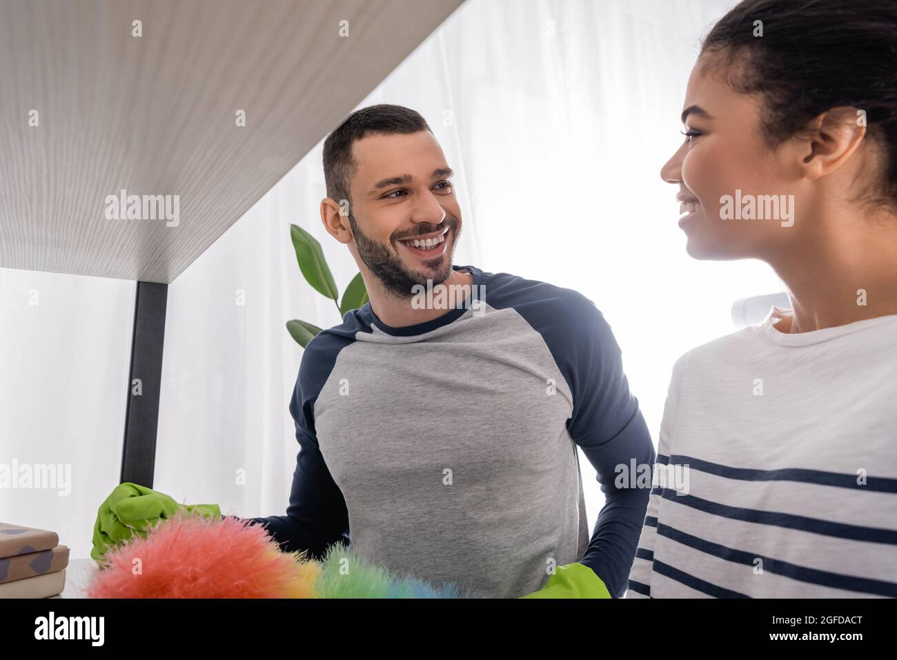 Interracial couple smiling at each other while cleaning cupboard Stock Photo