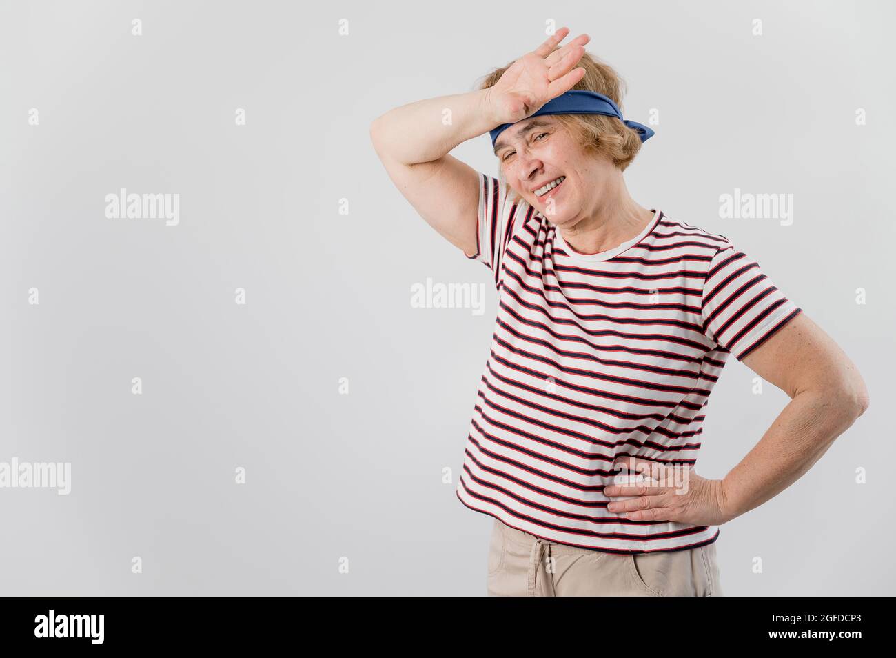 Elderly woman tiredly wipes sweat from her forehead after sports. Stock Photo