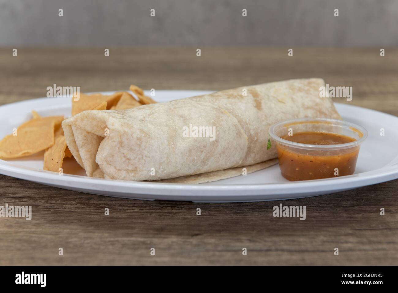 Hearty burrito wrapped in flour tortilla and served with chips and salsa on the side. Stock Photo