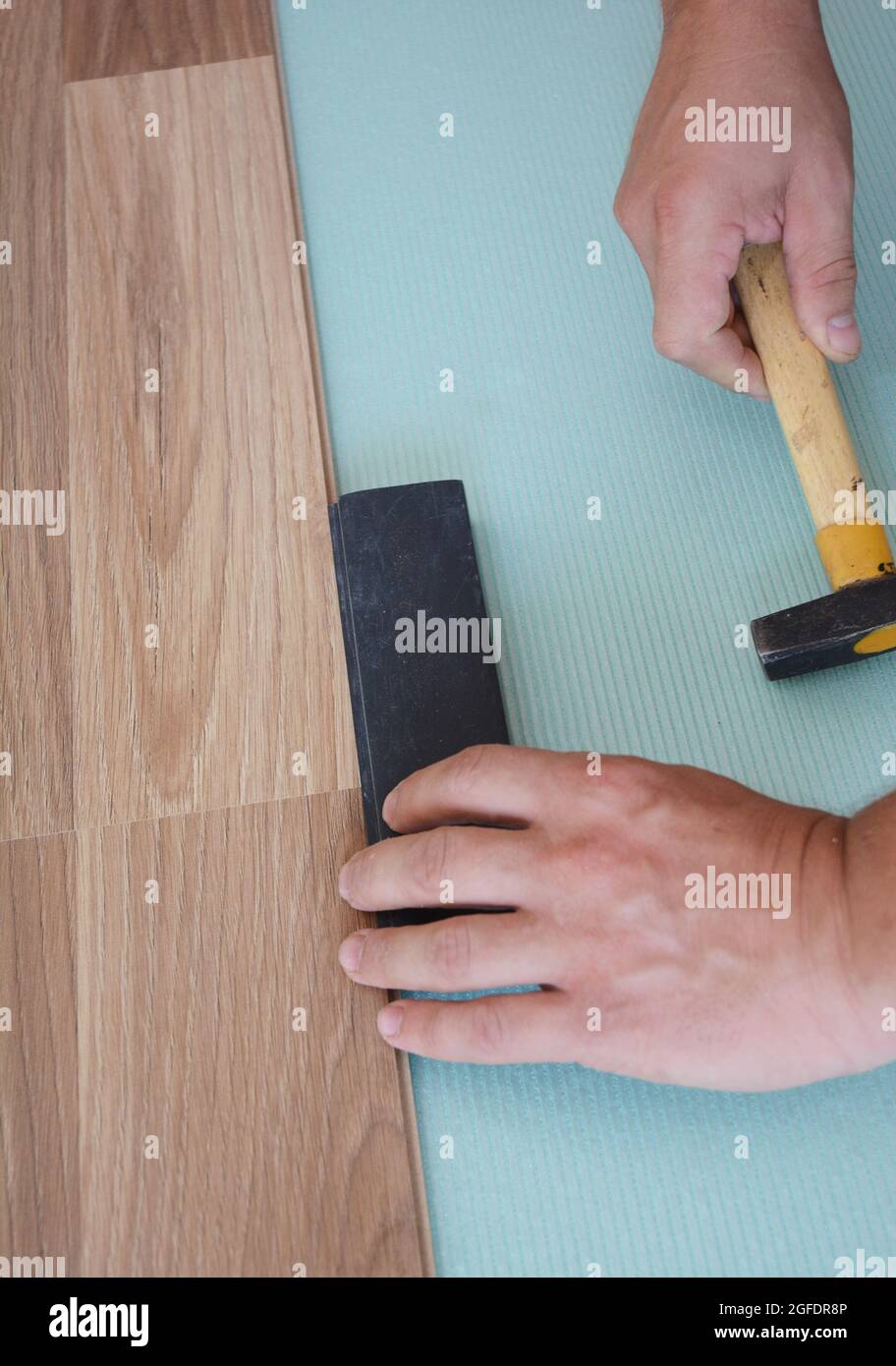 A handyman is installing a wood laminate flooring on the underlayment