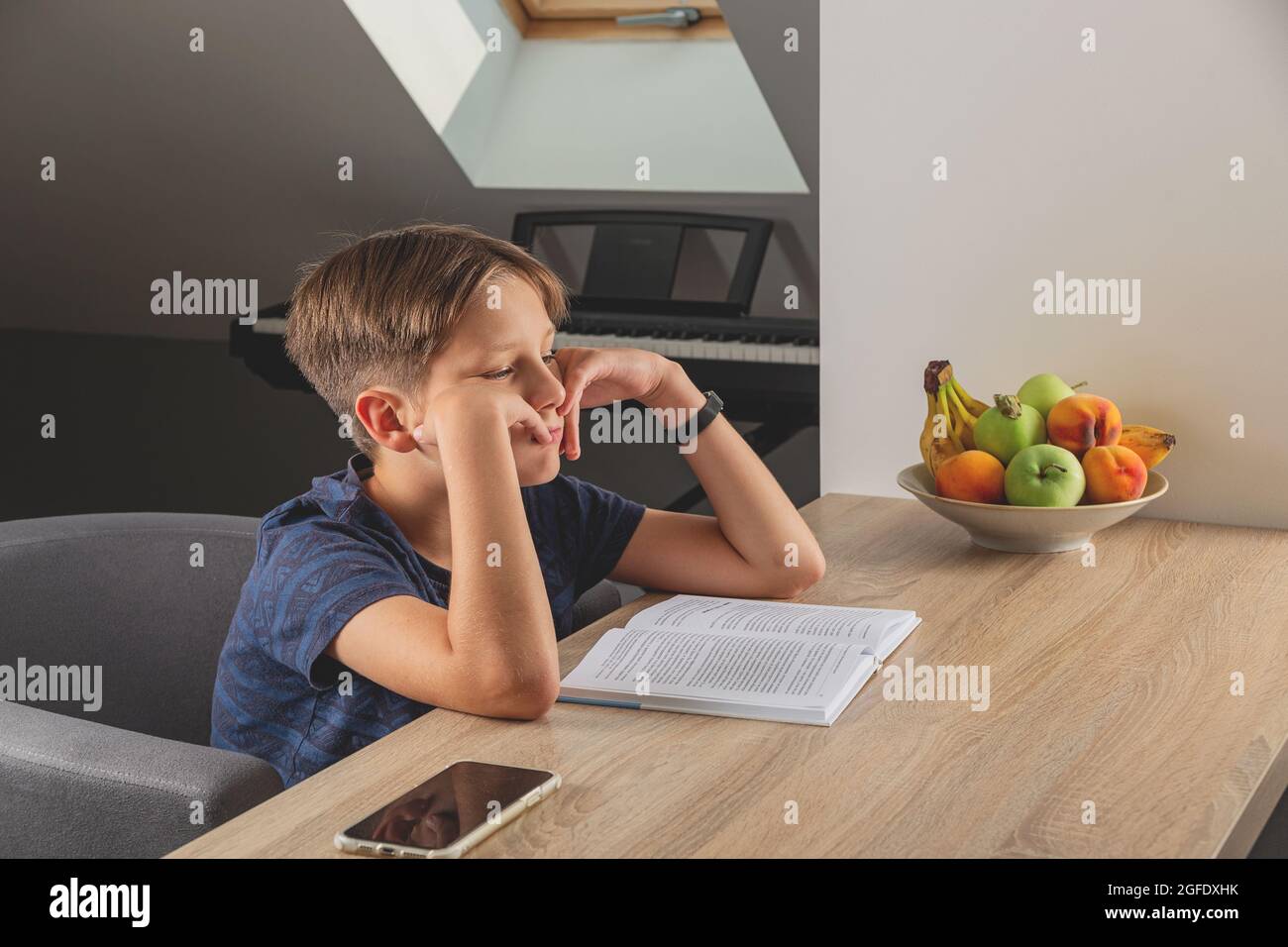 Kid boy doing homework at kitchen table with book Stock Photo