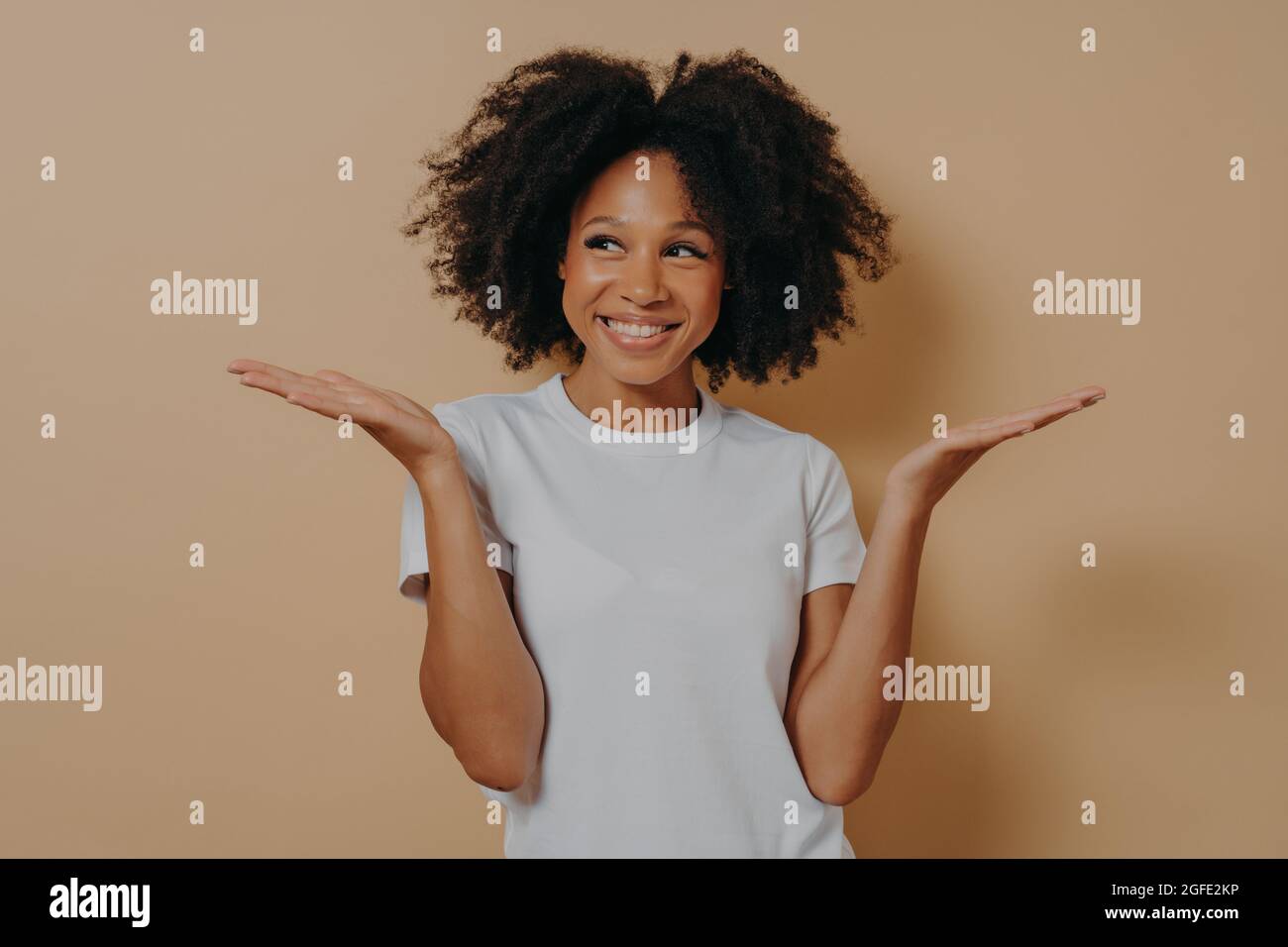 Young cheerful african woman spreading palms while posing isolated over beige background Stock Photo