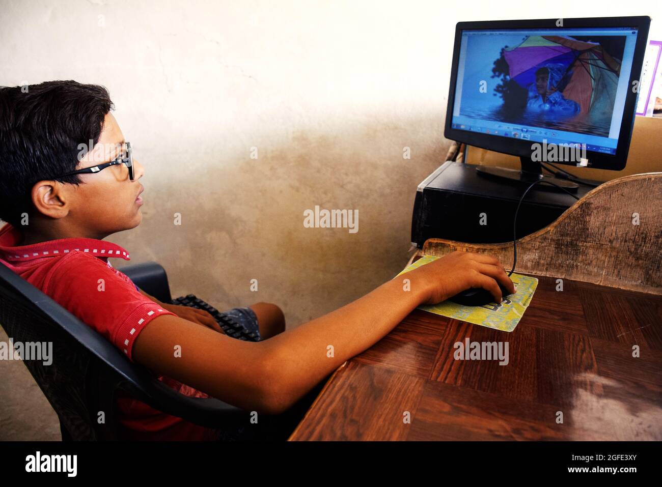 boy operating a computer using mouse and keyboard, He is looking at the picture in the computer system. Stock Photo