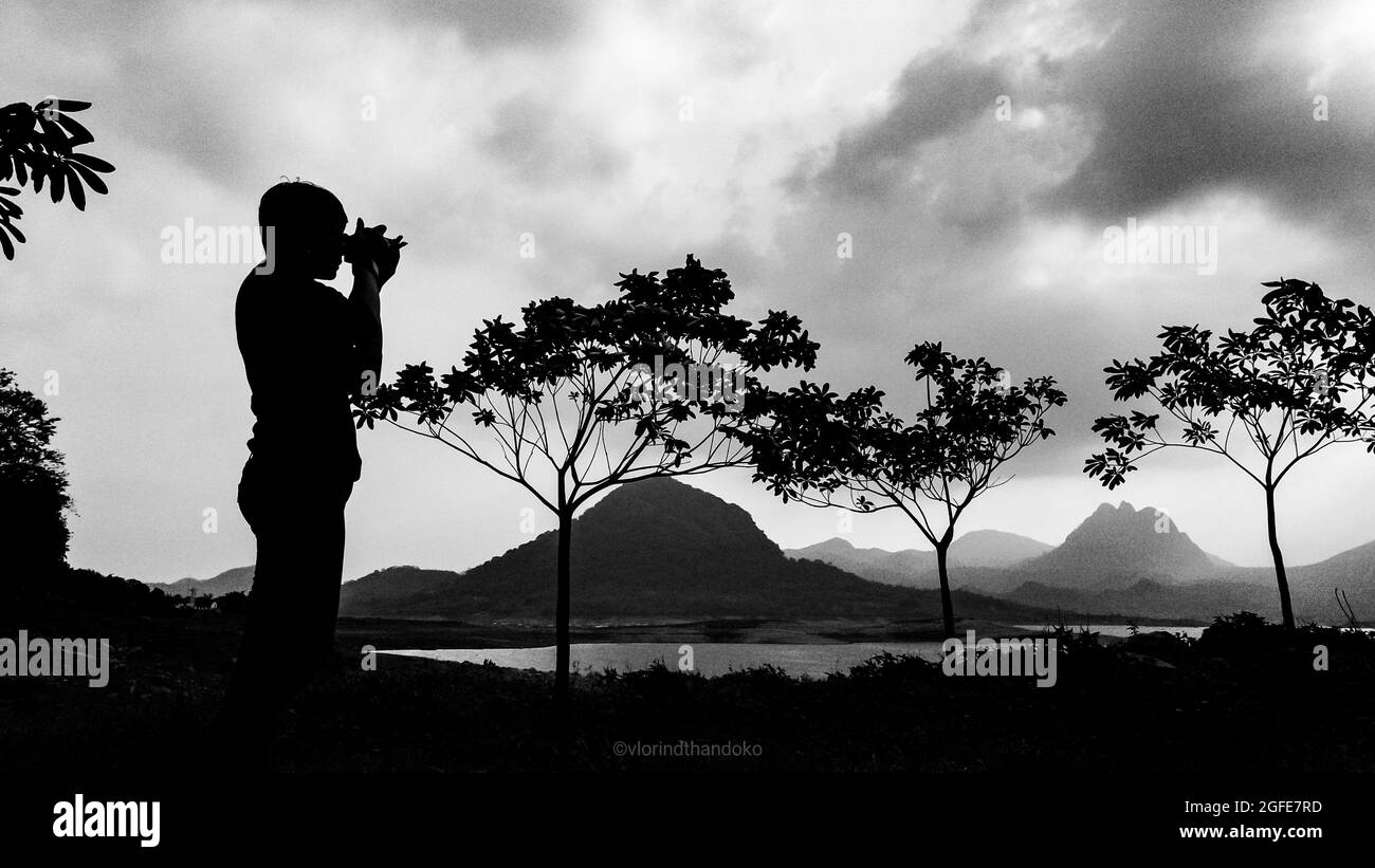 Photographer taking photo of landscape in Jatiluhur dam, west Java - Indonesia, trees and mountains in the background, dense clouds, black and white. Stock Photo
