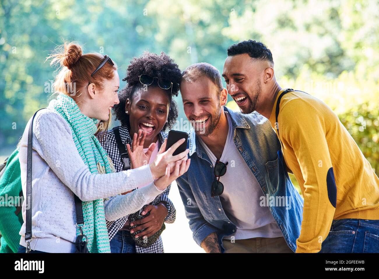 Happy young friends using smartphone in public park Stock Photo