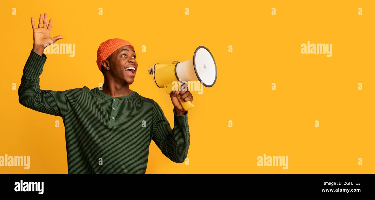 Portrait Of Joyful Black Guy With Megaphone In Hands Making Announcement, Excited African Man Holding Loudspeaker, Sharing News Or Interesting Offer Stock Photo