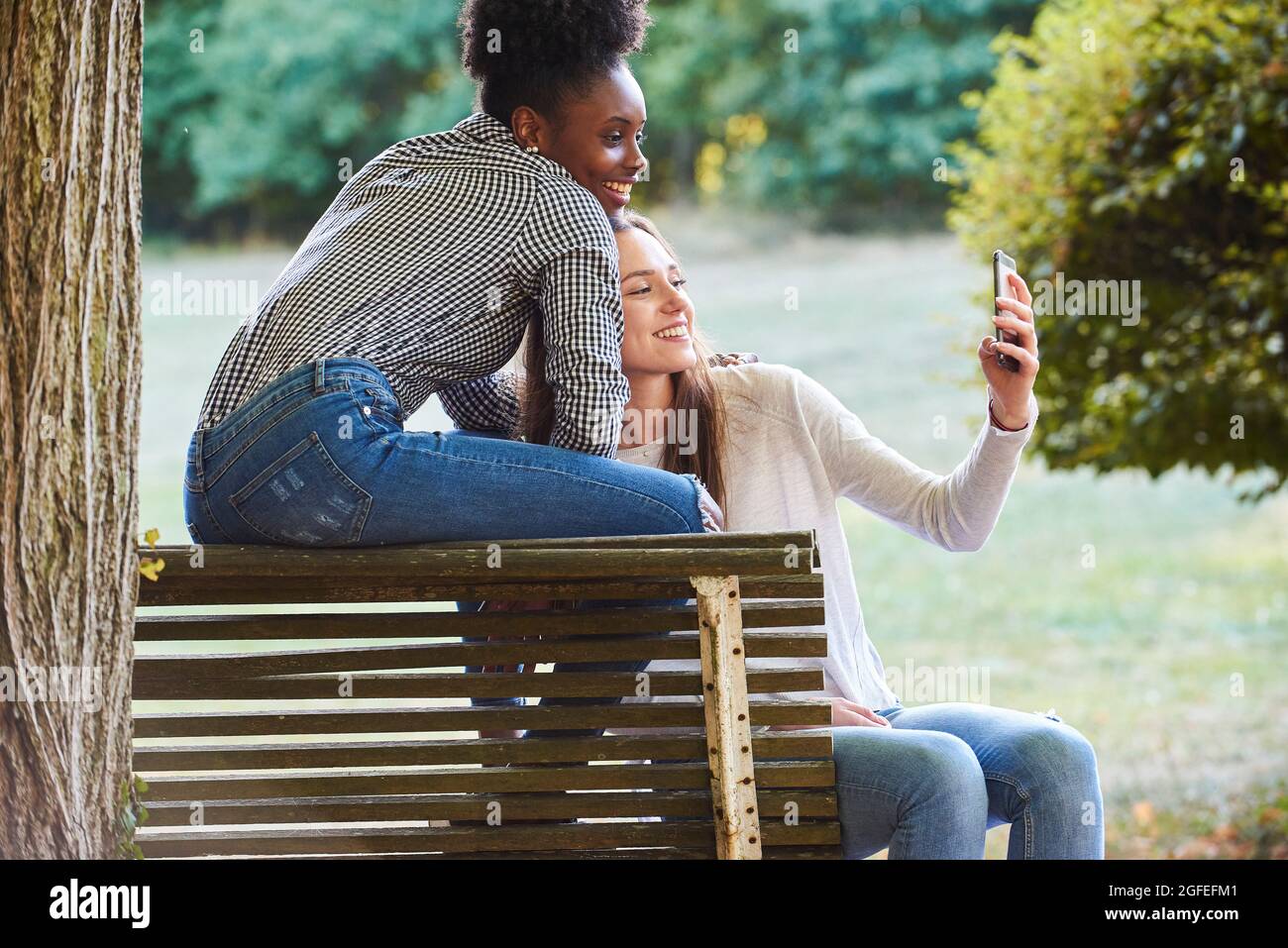 Smiling young friends talking selfie on smartphone in public park Stock Photo