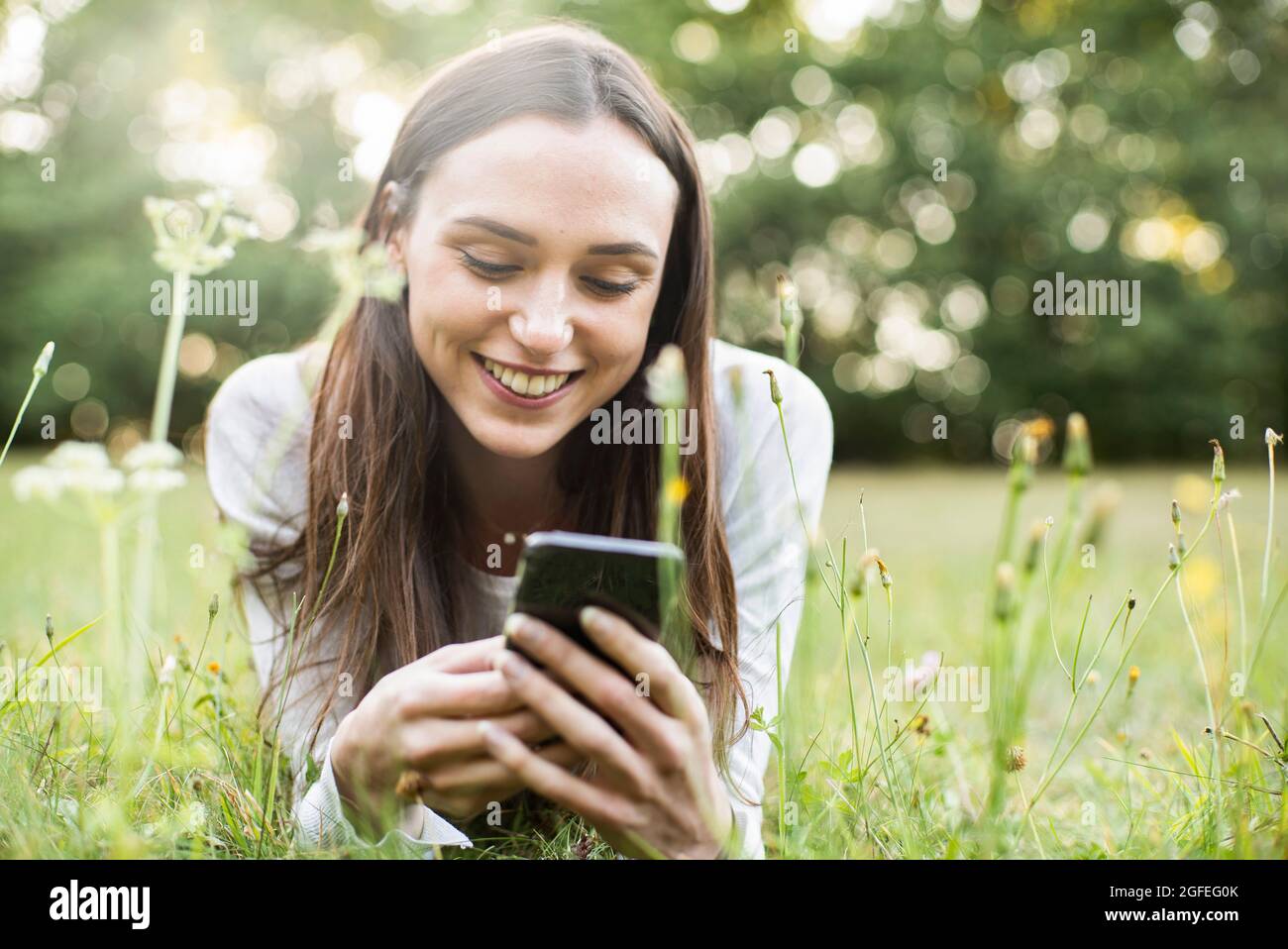 Young woman using smart phone while lying in park Stock Photo