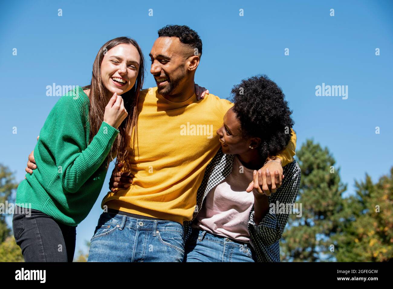 Smiling young friends standing with arm around in public park Stock Photo