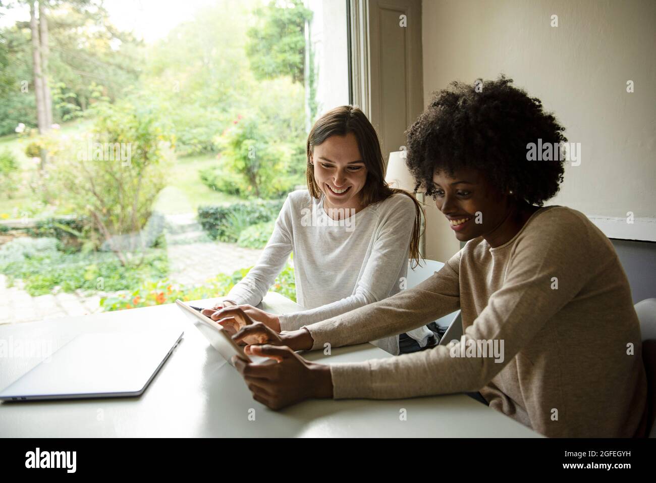 Smiling young women using digital tablet at home Stock Photo
