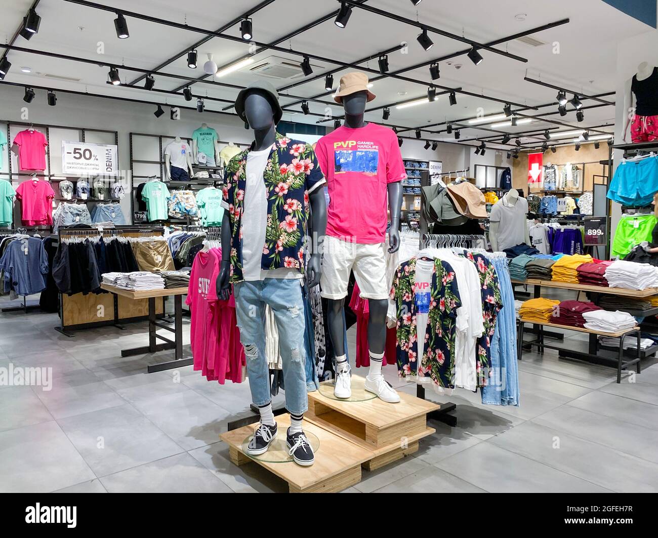 Moscow, Russia, June 2021: Men's Clothing Department. Two male mannequins in T-shirts, shorts, a Hawaiian shirt in the center of the store. Shelves wi Stock Photo