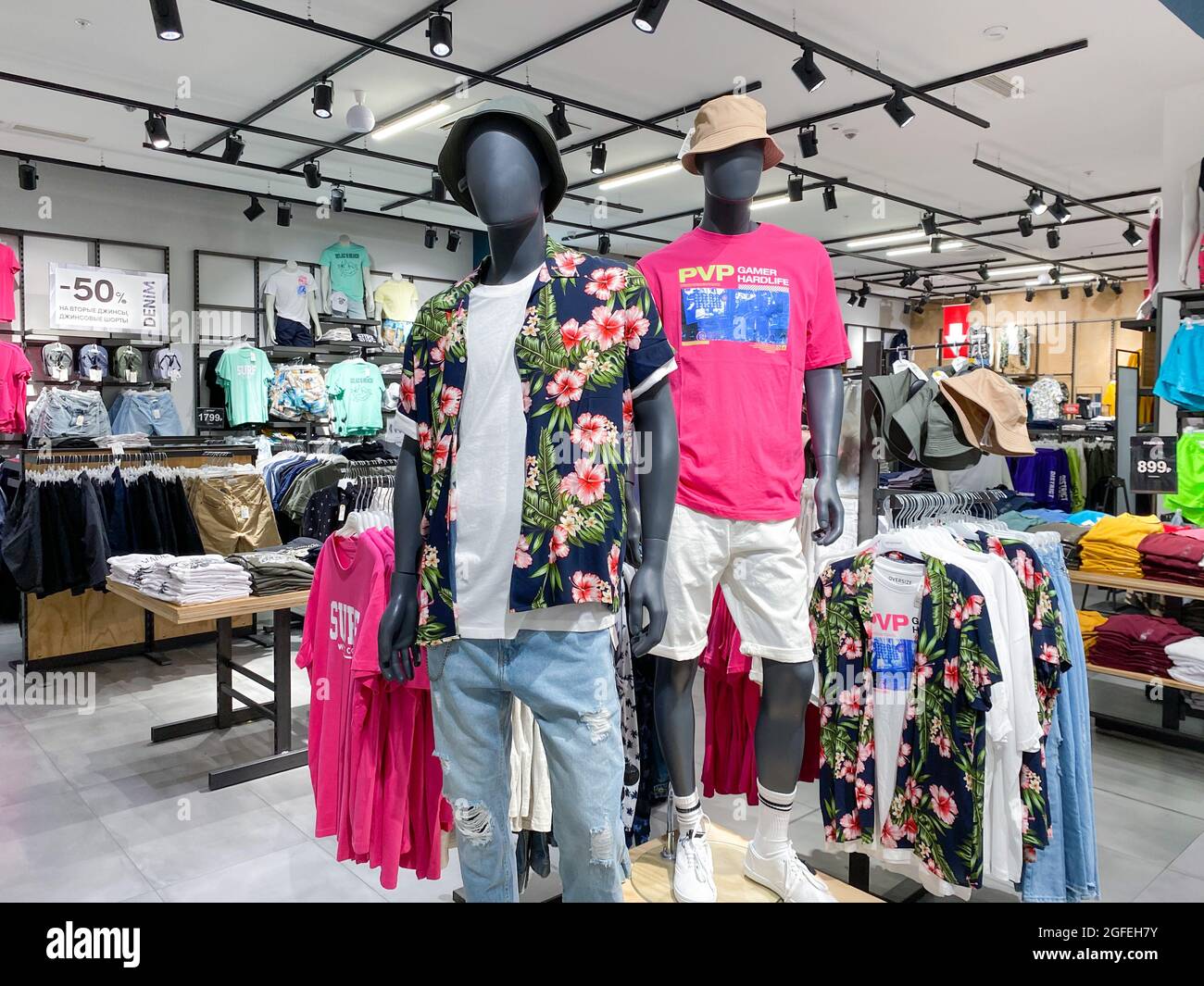 Moscow, Russia, June 2021: Men's Clothing Department. Two male mannequins in T-shirts, shorts, a Hawaiian shirt. Shelves with casual-style clothes are Stock Photo