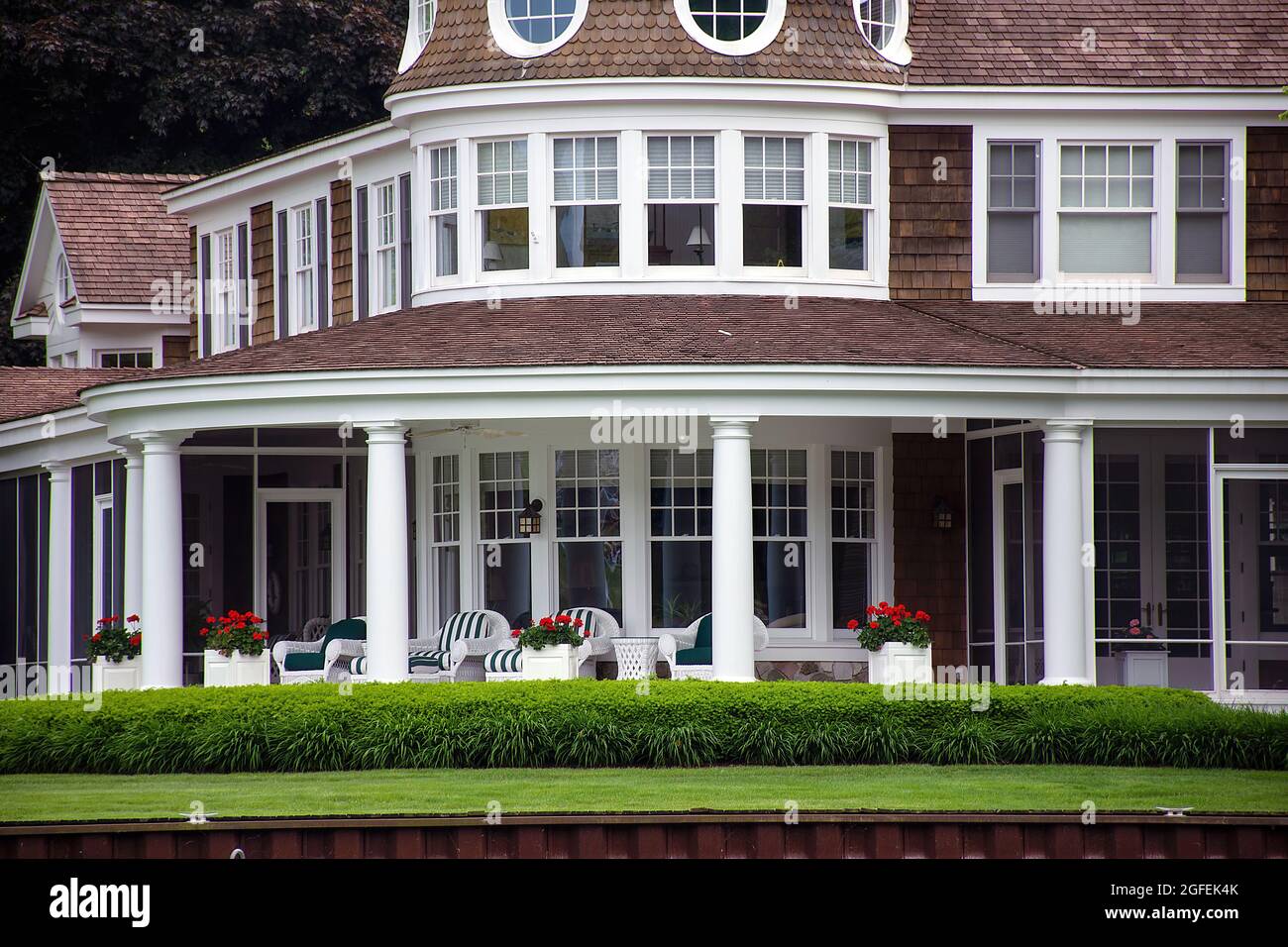 luxury summer home with white wicker furniture on a porch and red geraniums Stock Photo