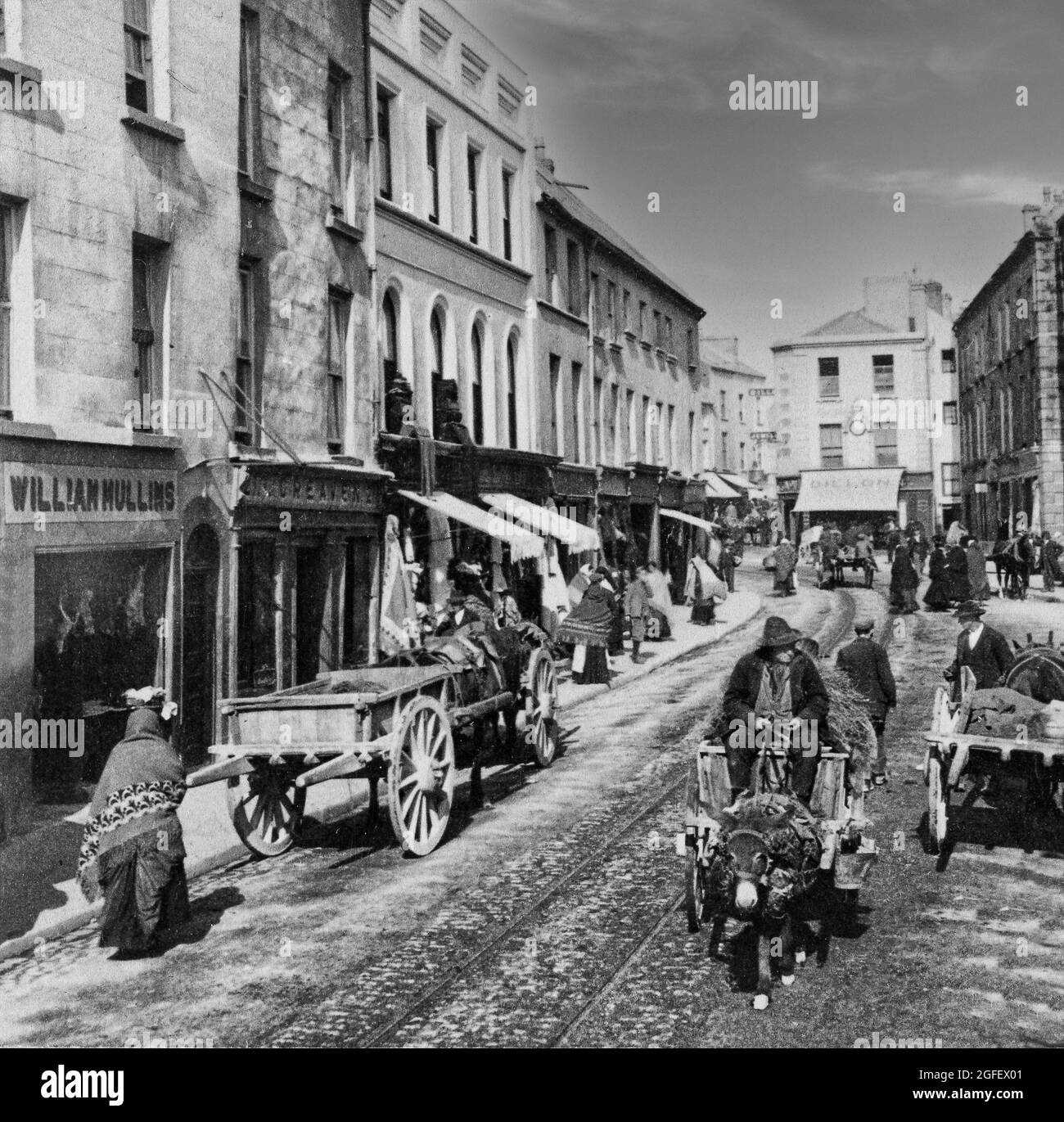 An early 20th century photograph of shoppers and locals in High Street in Galway City. Horse and donkey carts maneuvre around the tramlines running down the centre of the street. Stock Photo