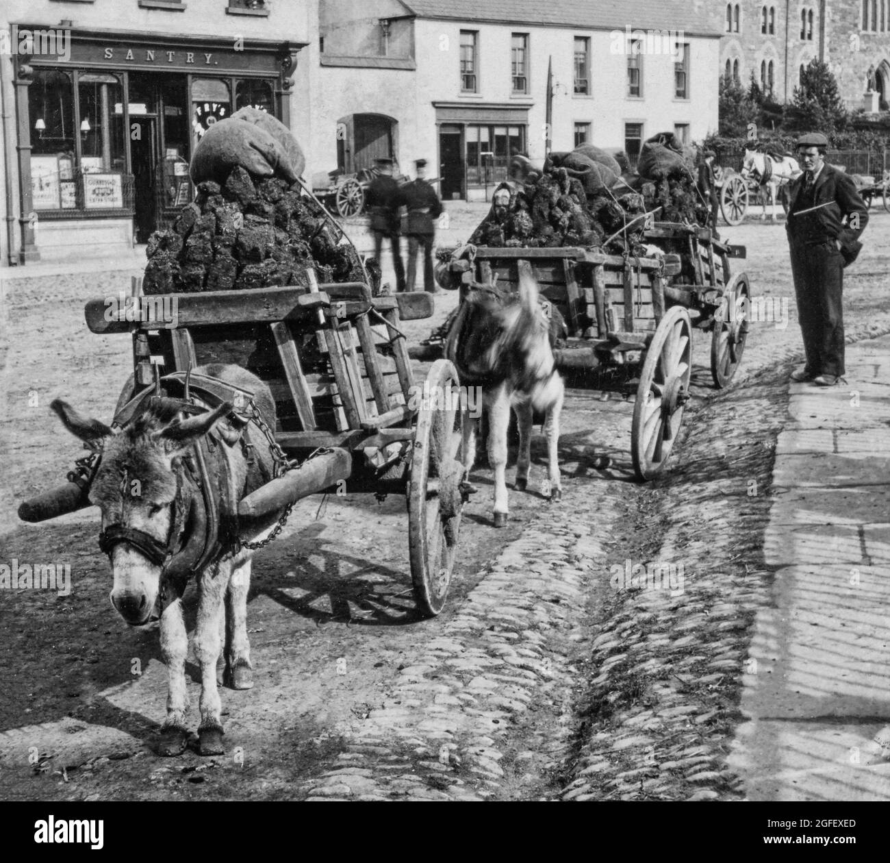 An early 20th Century photograph of two members of the RIC (Royal Irish Constabulary) passing donkey carts laden with turf (aka peat) in the Market Square, Killarney town, County Kerry, Ireland. Stock Photo