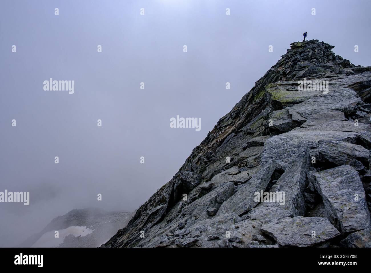 Climber on top of a rocky mountain surrounded by clouds Stock Photo