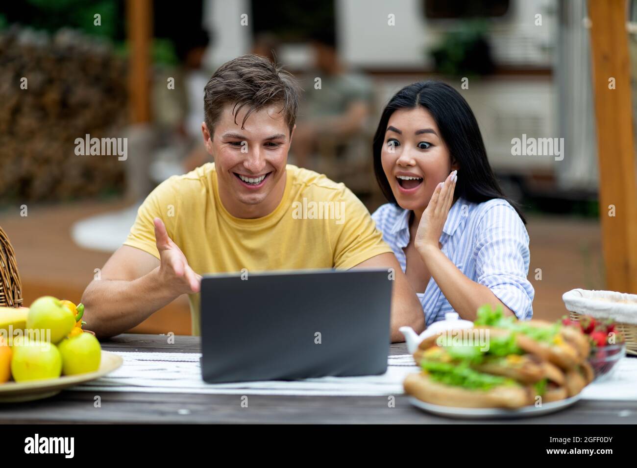 Excited young diverse couple using laptop near RV outdoors, chatting with friend on web, enjoying autumn camping trip Stock Photo