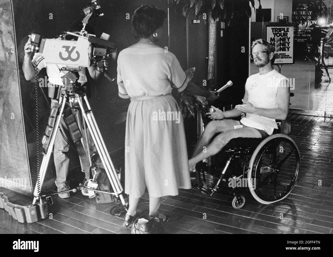 Austin Texas USA, 1994: Female television news reporter interviews man in wheelchair while cameraman records  the interaction. ©Bob Daemmrich Stock Photo