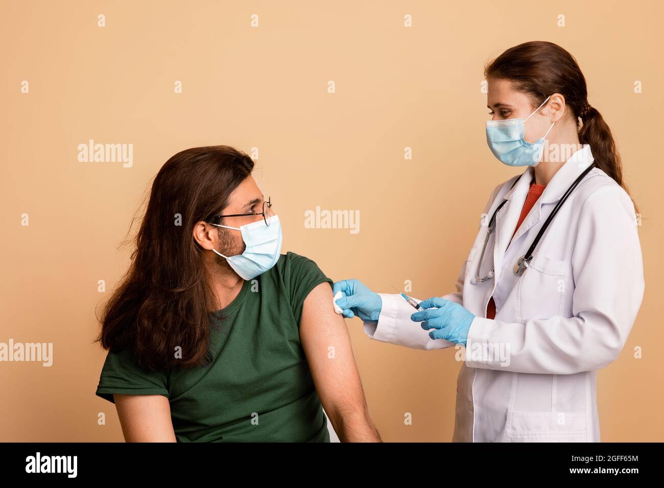 Female doctor making vaccination for long-haired indian guy Stock Photo