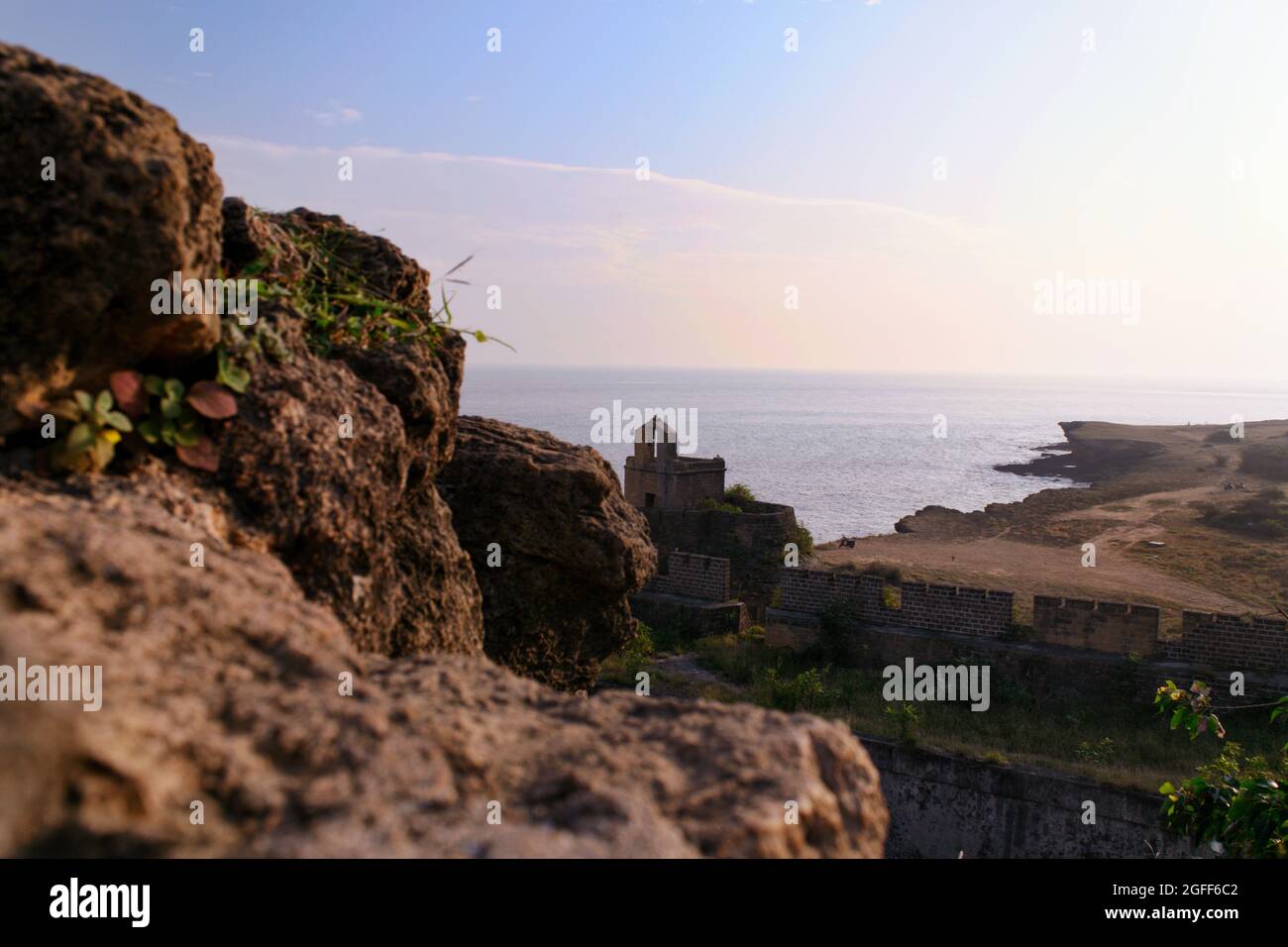 A Photograph of the Diu Coastline with the Sun setting into the horizon in the background and a coastal rock in the foreground. Stock Photo