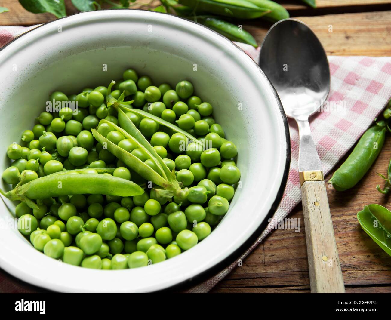 Fresh green peas in a white bowl, pods, on the table Stock Photo