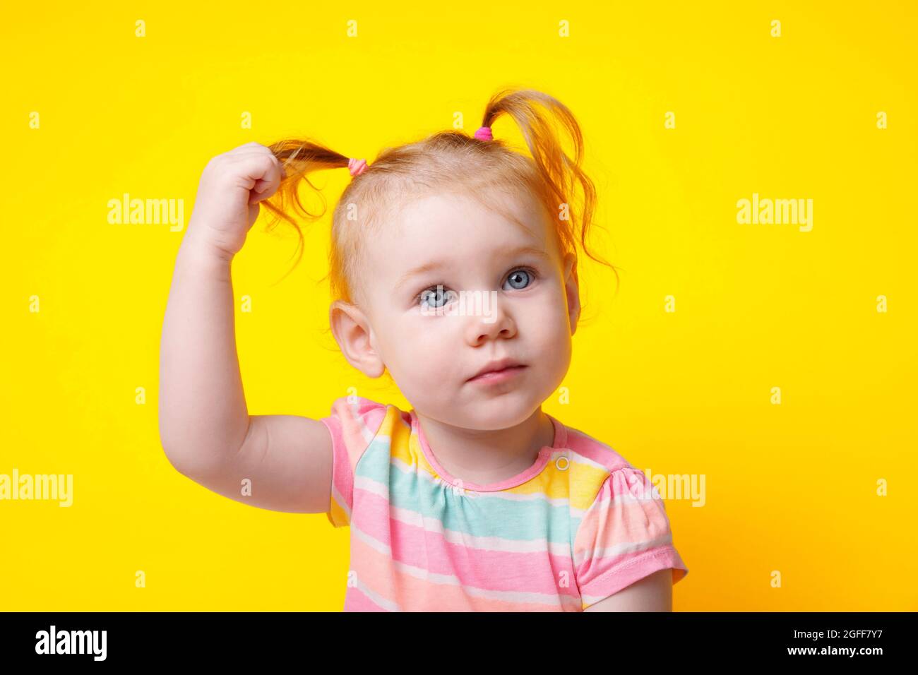 cute caucasian baby girl with ponytails over yellow background Stock Photo