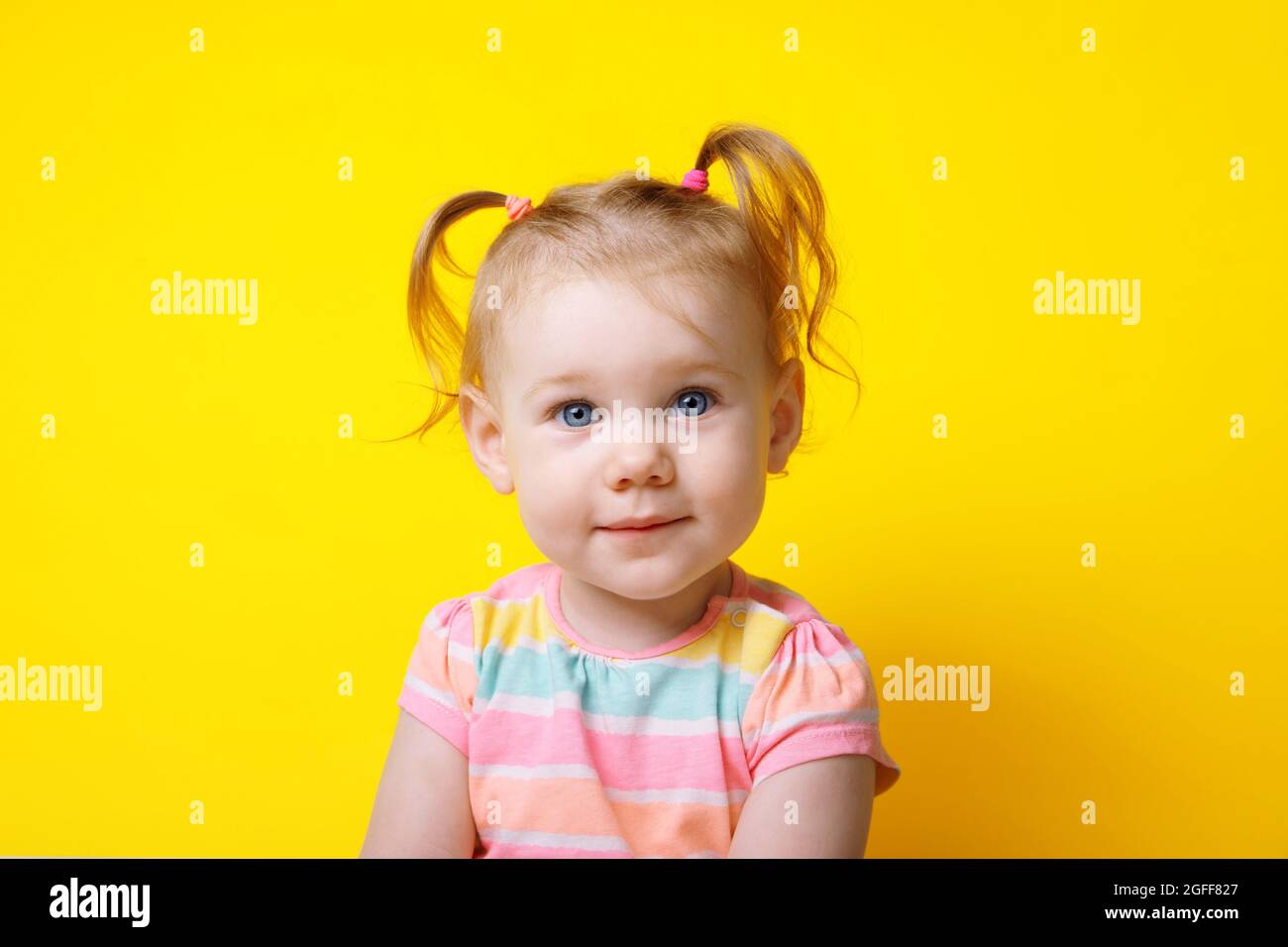 little caucasian girl smiling and looking at the camera over yellow ...