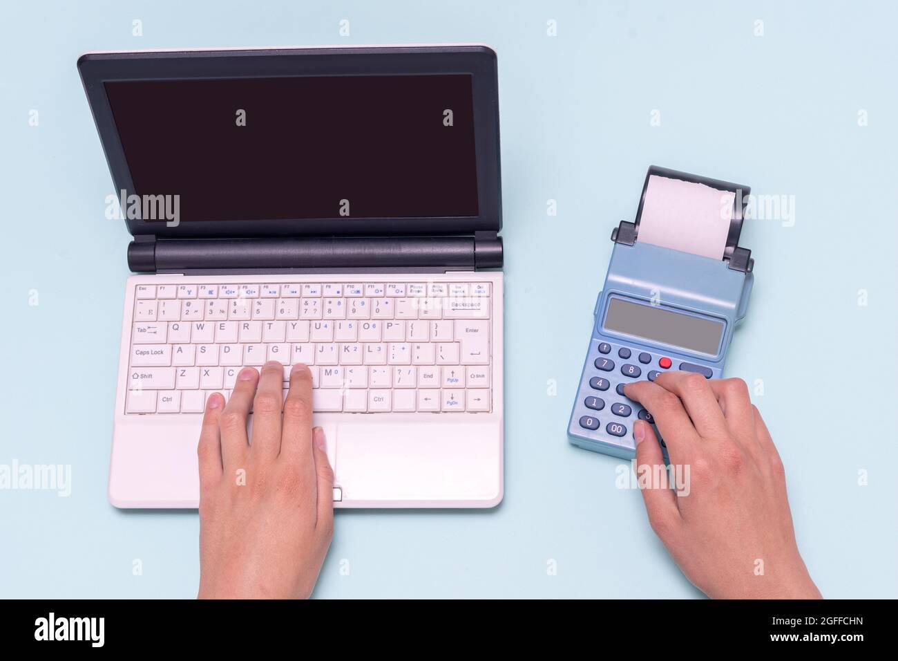 Hand typing on a laptop and a cash register on a blue background. Sales person entering amount on cash register in retail store. Online e-commerce sho Stock Photo