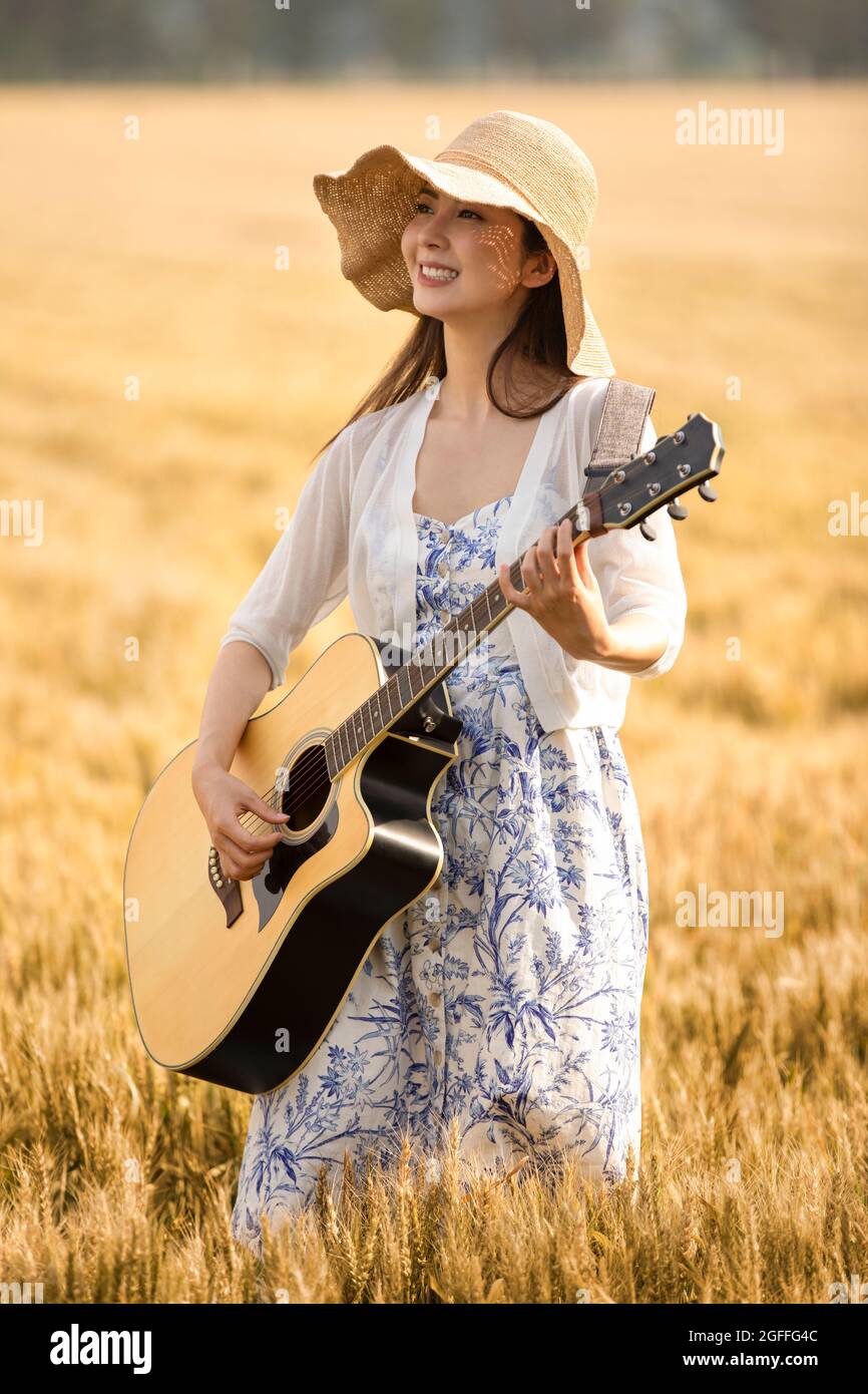 Happy young woman playing guitar in wheat field Stock Photo - Alamy