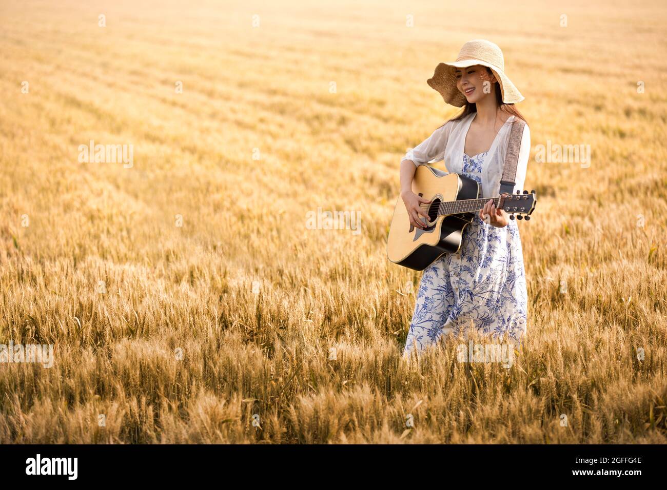 Happy young woman playing guitar in wheat field Stock Photo - Alamy