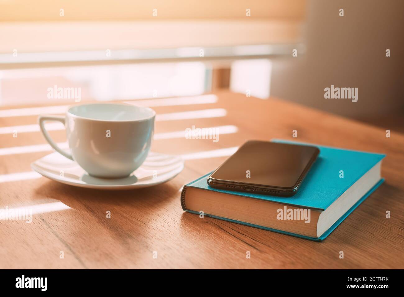 Cup of coffee, mobile smart phone and a book on the table in morning, selective focus Stock Photo