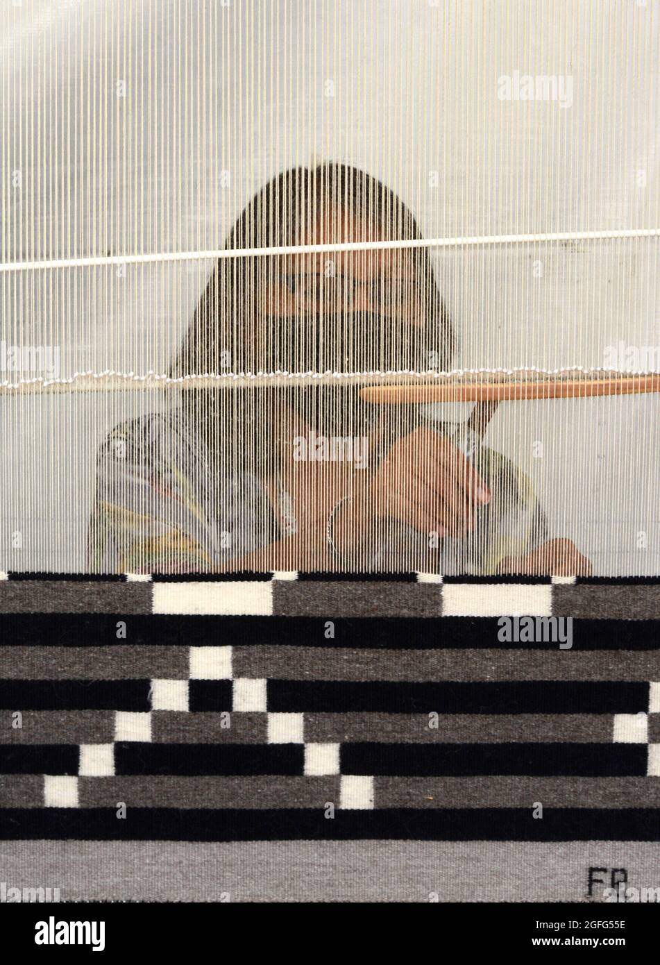 A Navajo Native American woman demonstrates the art of weaving a rug on a small loom at the annual Santa Fe Indian Art Market in New Mexico. Stock Photo