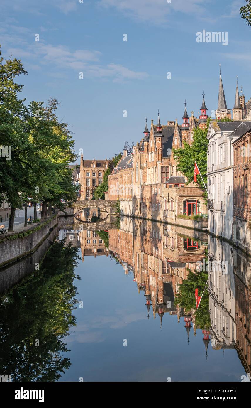 Brugge, Flanders, Belgium - August 4, 2021: Blinde Ezelstraat brick bridge and sunlighted palace building facades reflected in quiet Groenerei canal w Stock Photo