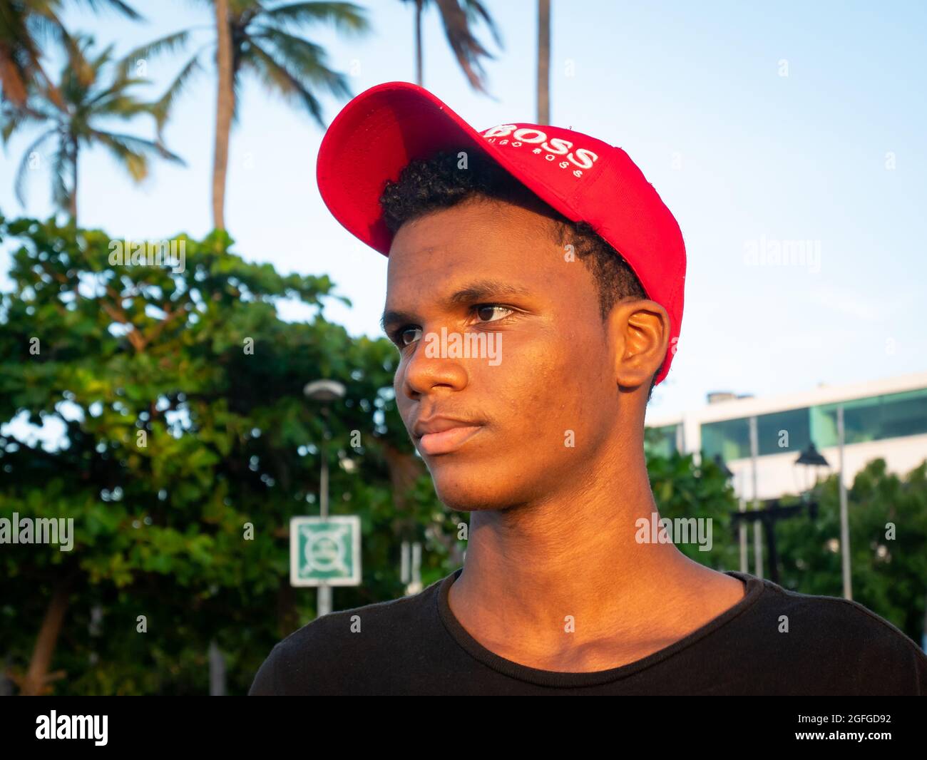 Riohacha, La Guajira, Colombia - May 26 2021: Portrait of a Young Latin Man with a Red Cap Looking at the Sunset with Palm Trees and Blue Sky in the B Stock Photo