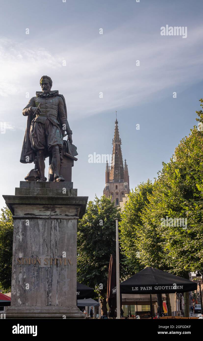 Brugge, Flanders, Belgium - August 4, 2021: Closeup of Simon Stevin bronze statue on gray pedestal with Notre Dame cathedral spire in back under blue Stock Photo