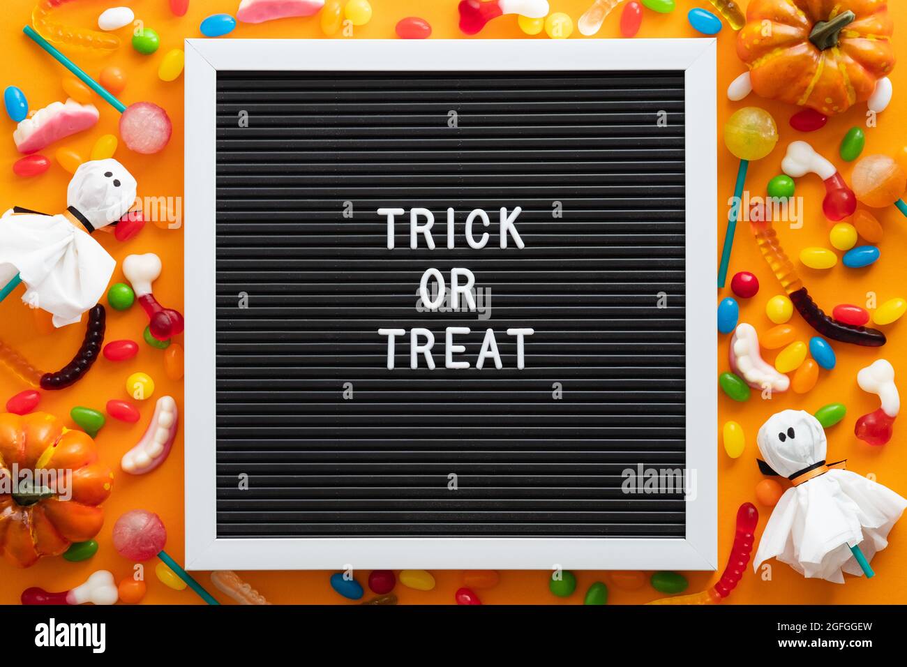 Trick or treat letter board with colorful Halloween candies and decorations on orange background. Flat lay, top view, overhead. Happy Halloween concep Stock Photo