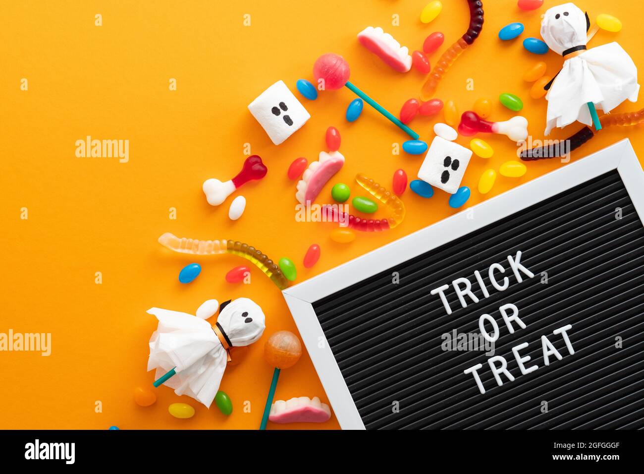 Halloween sweets and letter board with text Trick Or Treat on orange background. Happy Halloween holiday concept. Flat lay, top view, overhead. Stock Photo