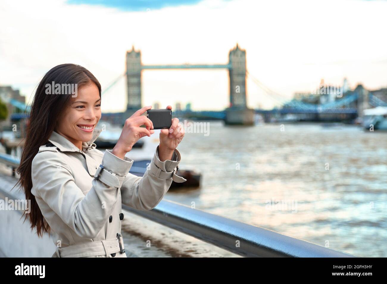 London woman tourist taking photo of Tower Bridge. London woman taking photos with mobile smart phone camera. Girl enjoying view over the River Thames Stock Photo