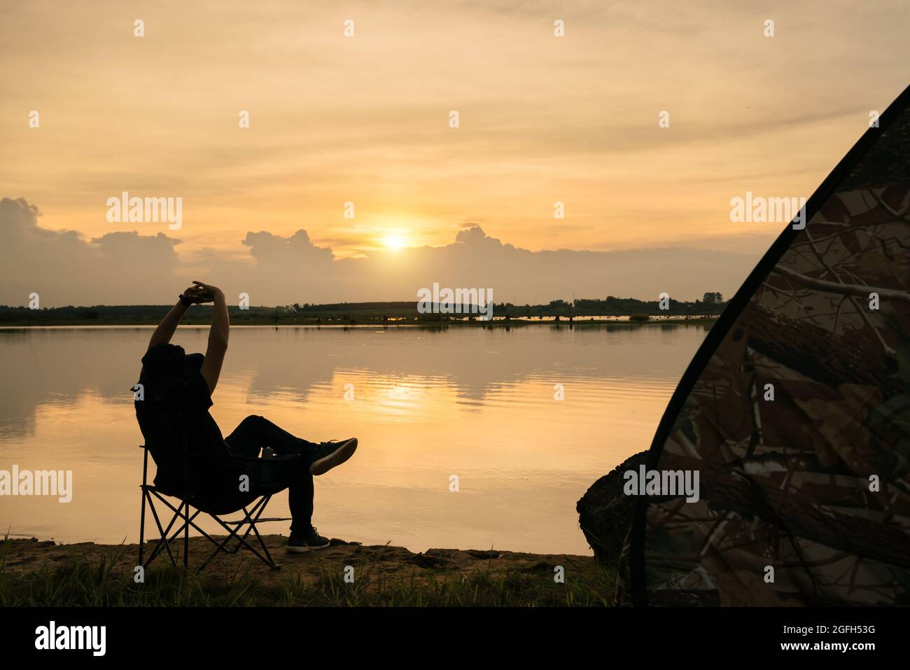 Asian young man traveler relax, enjoying sunset scenery view of the river landscape, sitting in touristic chair. Travel camping and adventure lifestyl Stock Photo