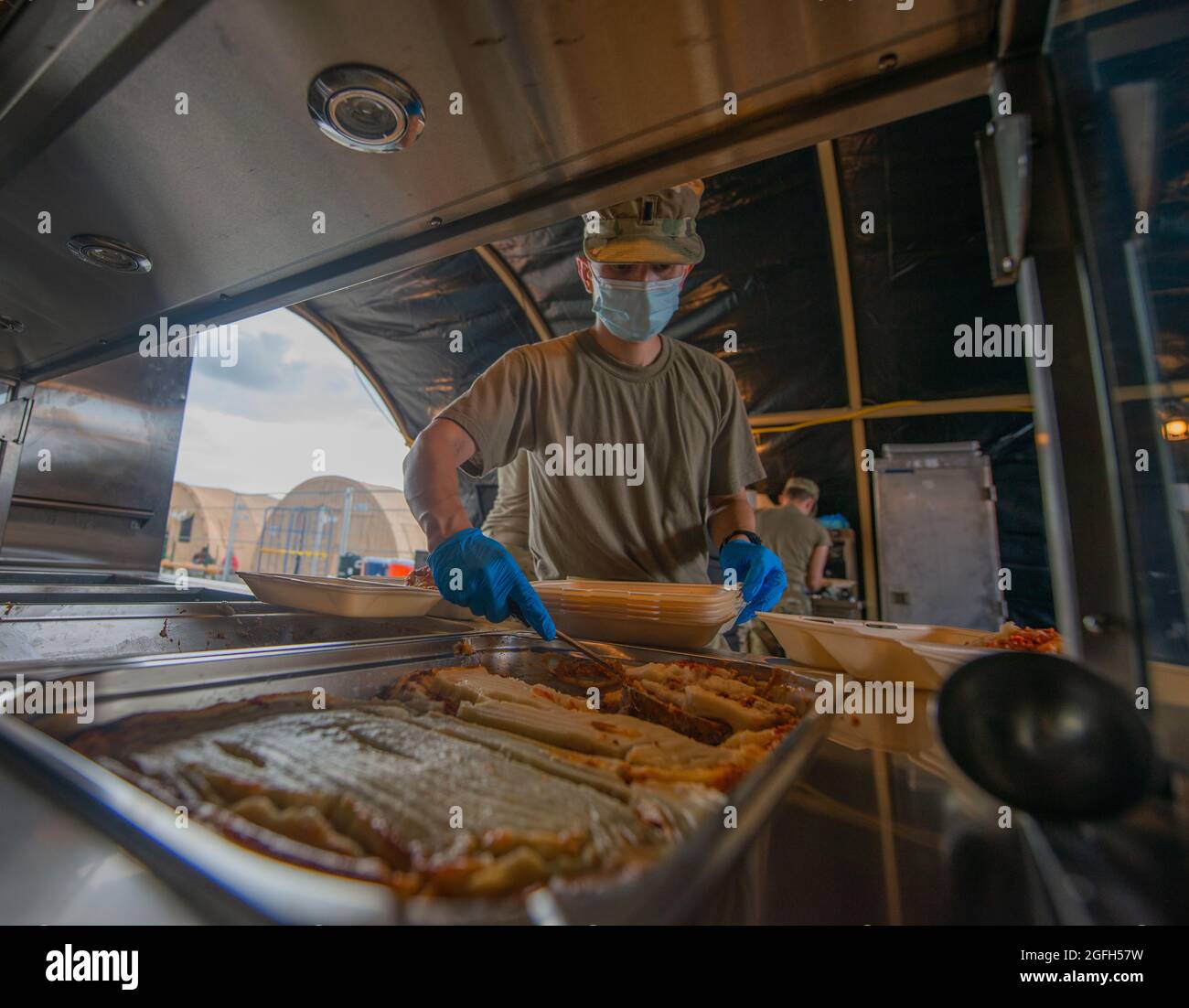 U.S. Air Force 1st Lt. Brandon Hosley, 691st Cyberspace Operations Squadron chief of weapons and tactics, prepares to serve a meal to evacuees at Ramstein Air Base, Germany, Aug. 24, 2021. U.S. Airmen work non-stop to provide thousands of meals to evacuees daily. Ramstein, a transit location for evacuees from Afghanistan, is providing temporary lodging, food, medical services and treatment while they await transportation to more permanent resettlement locations. Ramstein Air Base transformed into U.S. European Command’s primary evacuation hub supporting one of the largest, most complex humanit Stock Photo
