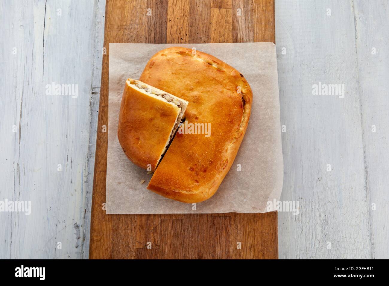 From above yummy cut meat pie served on parchment on lumber chopping board on table Stock Photo