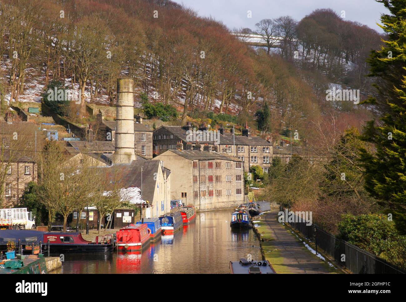 Tree covered hills with a dusting of snow, old mills and colourful long boats on the Rochdale Canal in Hebden Bridge, West Yorkshire, England Stock Photo