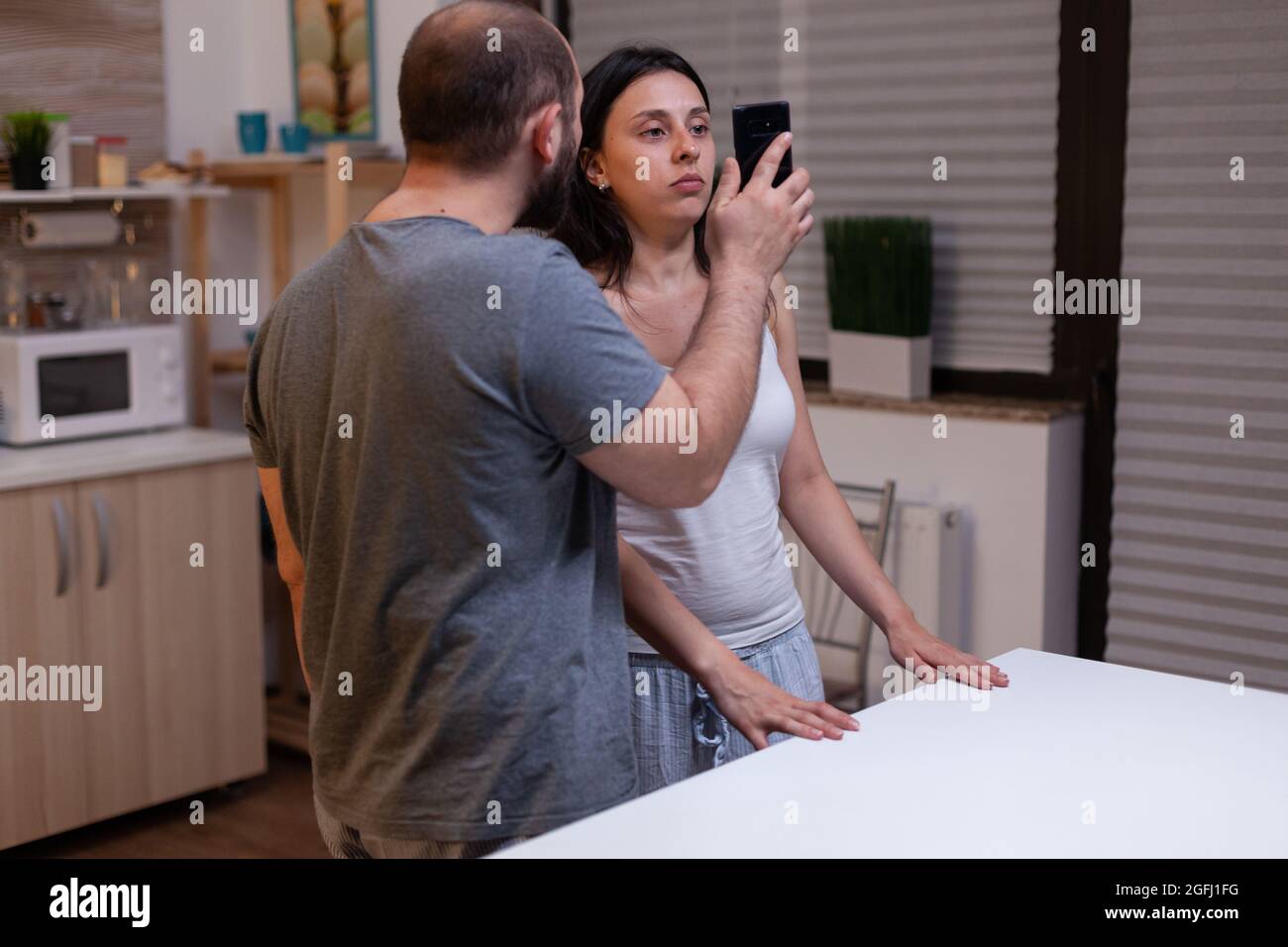 Angry jealous husband cheated by unhappy wife, couple fighting because of secret text messages with lover. Man showing smartphone with cheating proof to woman. Marriage infidelity. Stock Photo